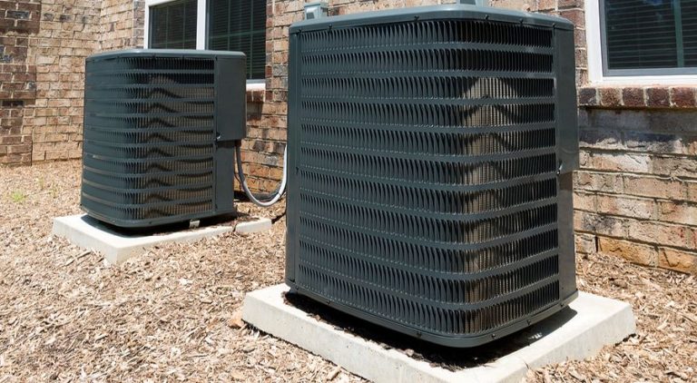 Air conditioning unit on top of a bed of mulch and hooked up to power a residential building.